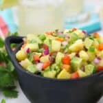 A close up shot of mini cast iron dish filled with pineapple salsa, it's got gorgeous color and there's some margaritas blurred out in the background