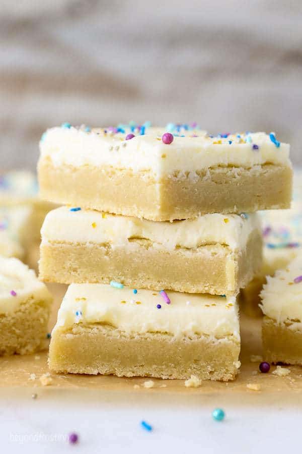 A stack of 3 sugar cookie bars with vanilla frosting sitting on a piece of brown parchment paper