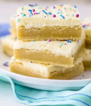 A stack of 3 sugar cookie bars with vanilla frosting and colorful blue and purple sprinkles on top