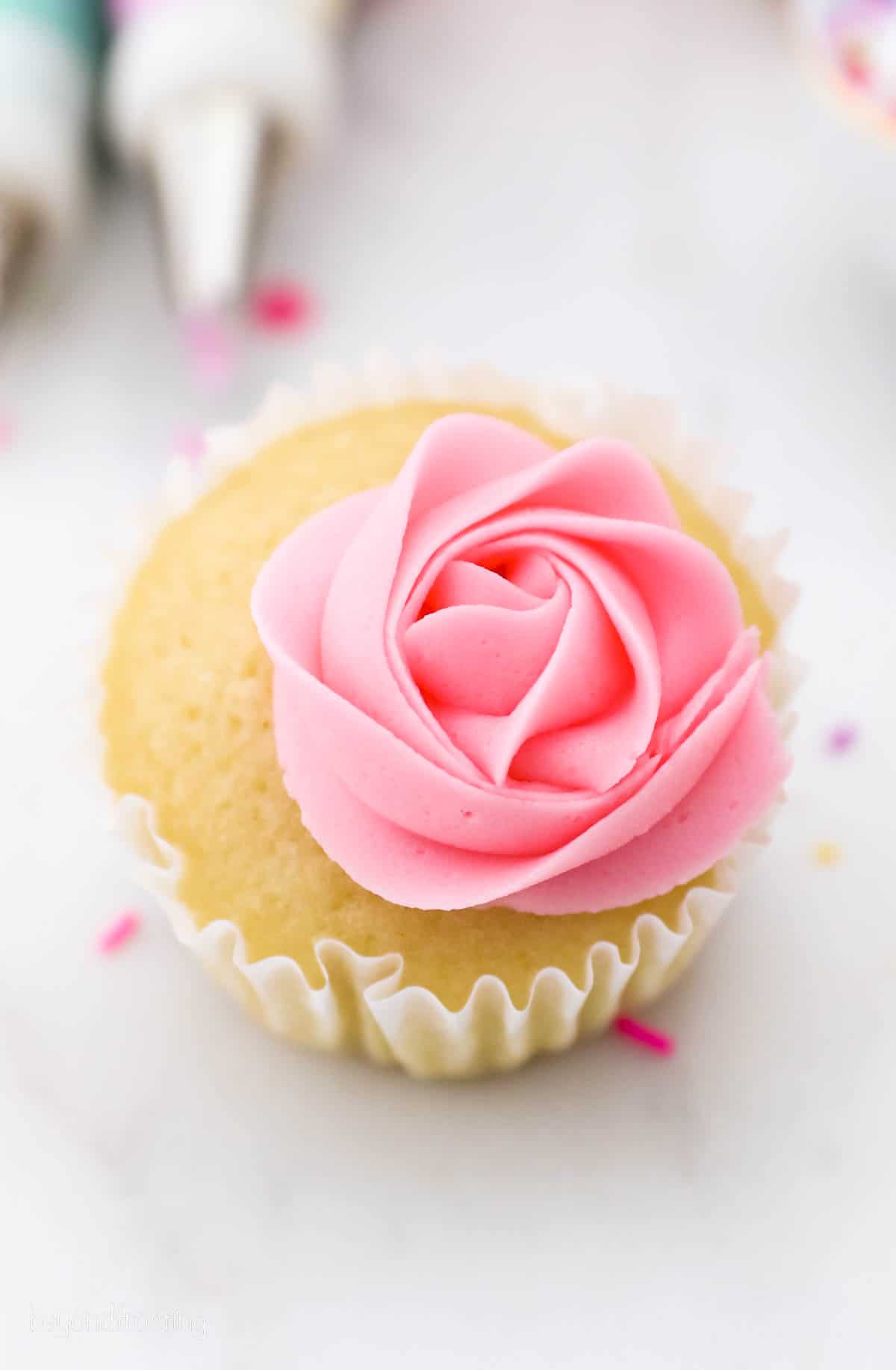 A vanilla cupcake topped with a pink buttercream rose.