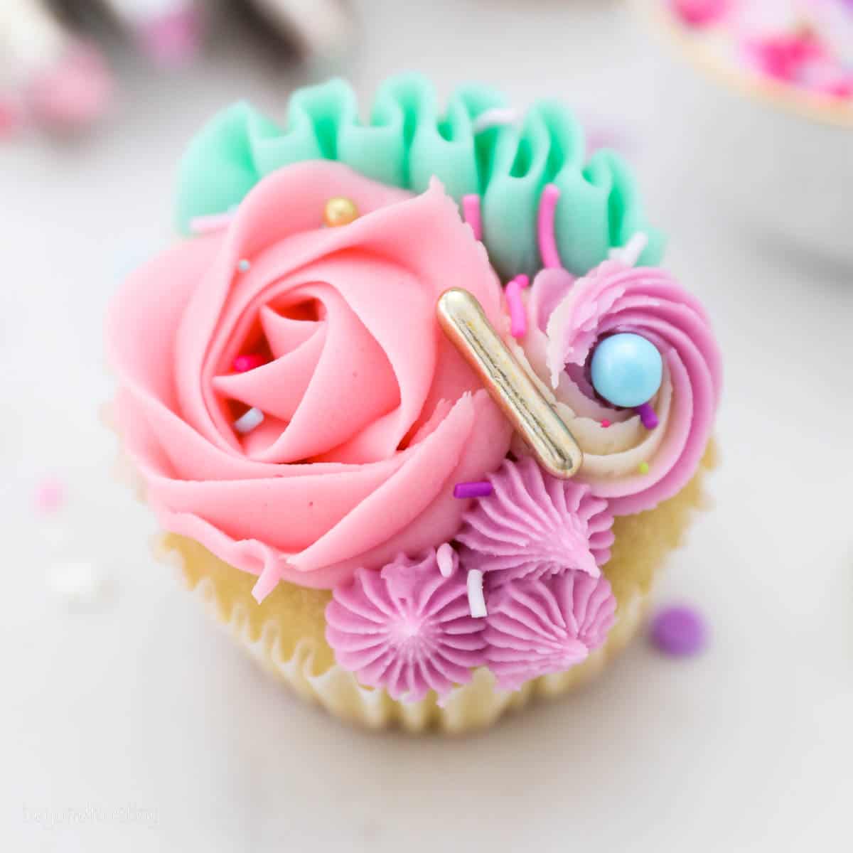 Overhead view of a unicorn cupcake decorated with pink, teal, and purple frosting roses and swirls.
