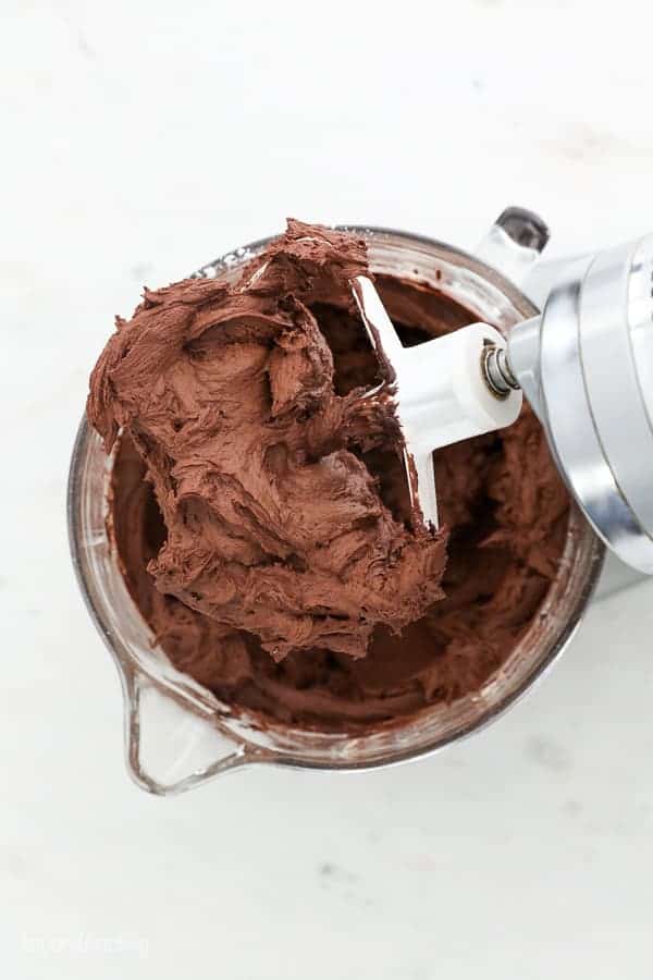 A spatula filled chocolate chocolate frosting sitting overtop of a glass mixing bowl