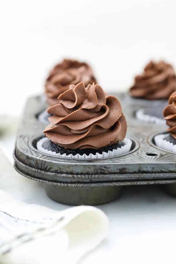 A vintage cupcake pan with chocolate cupcakes topped with a silky milk chocolate frosting
