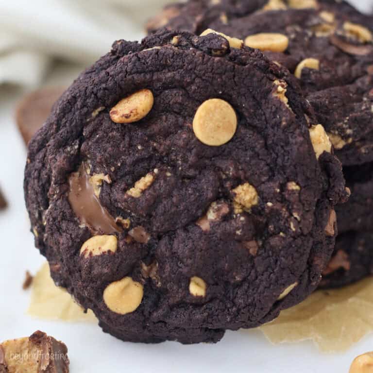 A chocolate peanut butter cookie propped upright against a stack of cookies on a countertop.