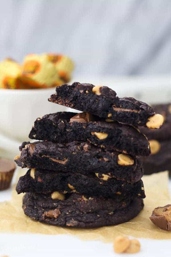 A big stack of of peanut butter cup stuffed chocolate cookies. The cookies are all torn in half revealing the fudgy middle.