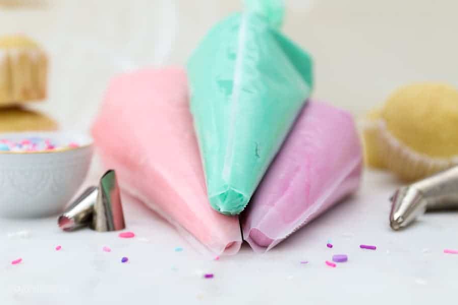 3 piping bags filled with colorful frosting: teal, link and purple