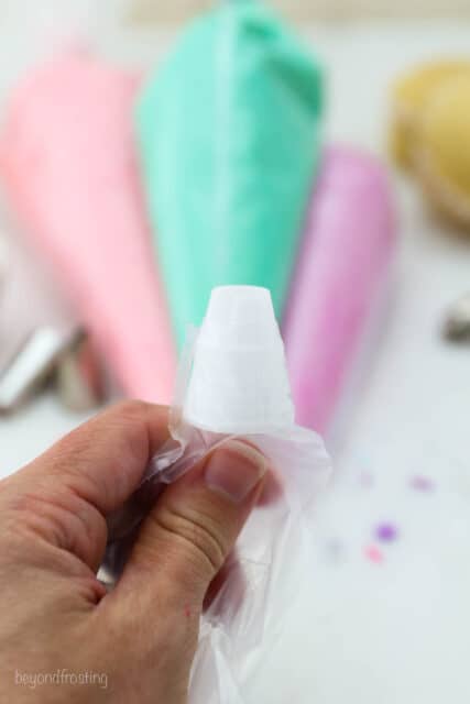 A hand holds the tip of a piping bag fitted with the larger piece of a coupler set.