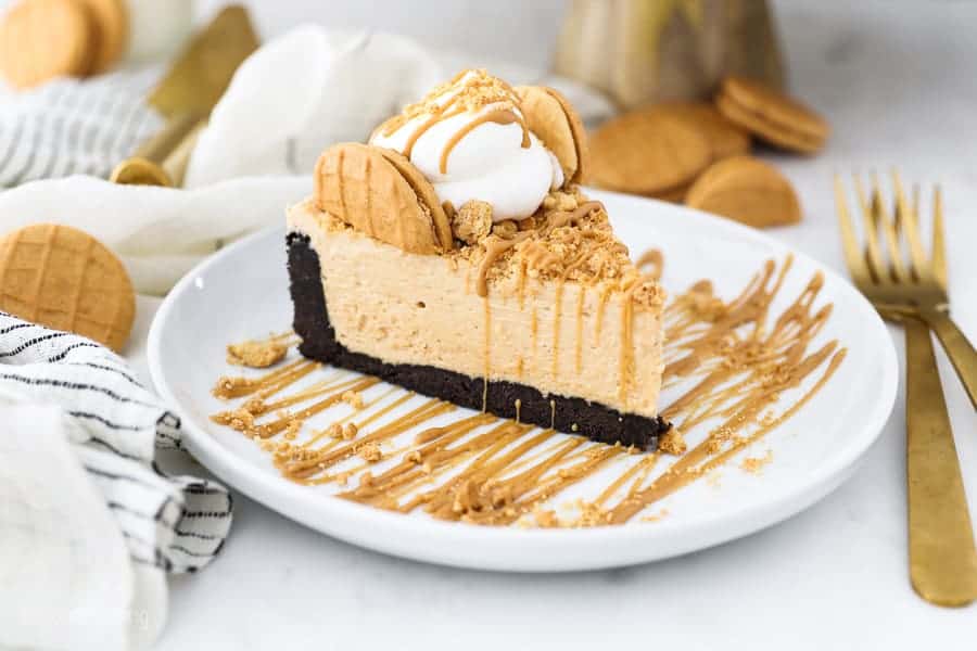 A gorgeous slice fluffy peanut butter pie on a white plate. There's two gold fork and some Nutter Butter cookie scattered around