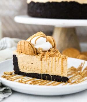 A close up shot of a slice of fluffy peanut butter pie on a white rimmed plate. There's a cake stand in the background with the pie sitting on it. It has an Oreo crust.