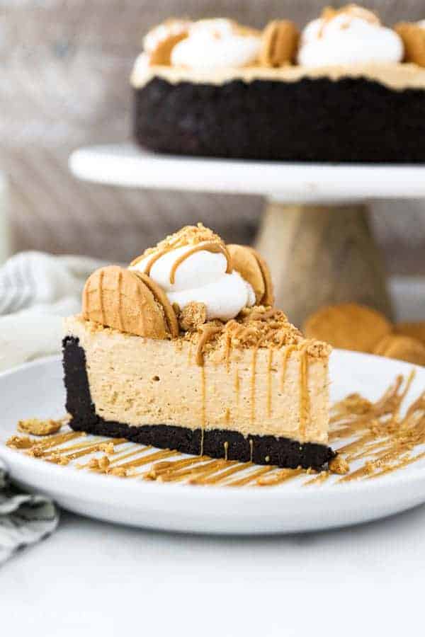 A close up shot of a slice of fluffy peanut butter pie on a white rimmed plate. There's a cake stand in the background with the pie sitting on it. It has an Oreo crust.