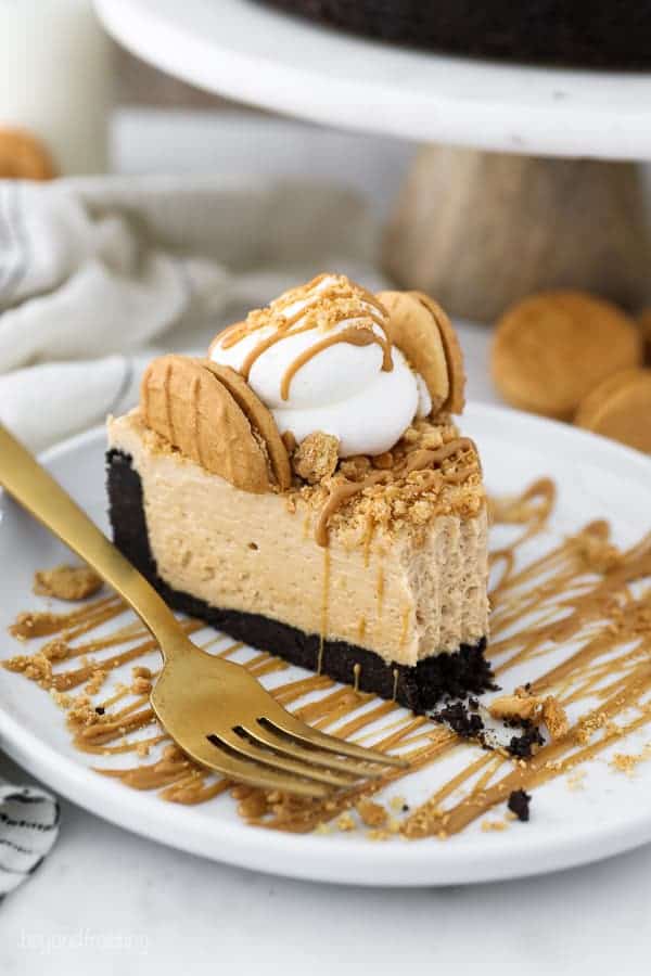 A white rimmed plate with a big slice of peanut butter pie it drizzled with peanut butter, crushed cookies and whipped cream. There's one bite missing from the slice of pie.