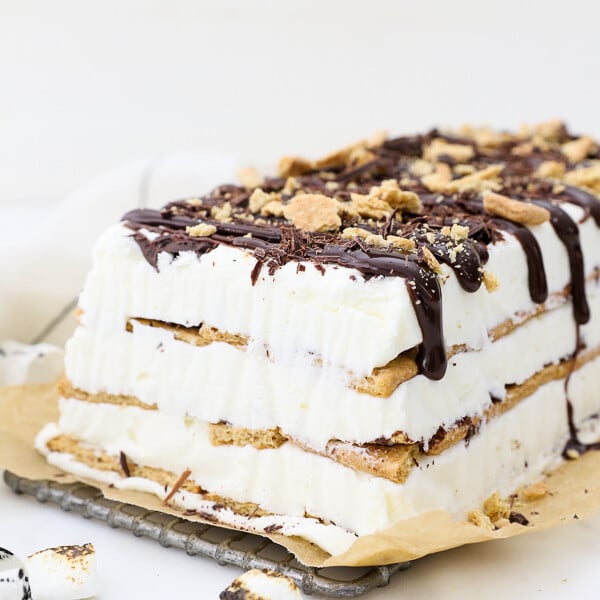 A sideview of the layered s'mores ice cream cake, with graham crackers and a no-churn ice cream. There's chocolate sauce dripping down the side and crushed graham crackers on top.