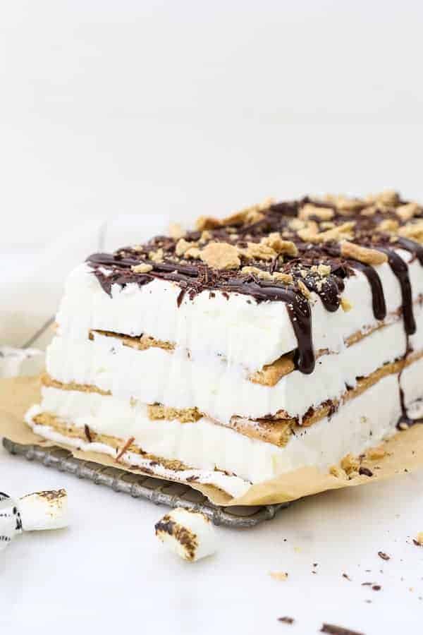 A sideview of the layered s'mores ice cream cake, with graham crackers and a no-churn ice cream. There's chocolate sauce dripping down the side and crushed graham crackers on top.