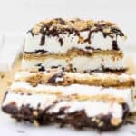 A head on shot of a layered s'mores ice cream cake, there's 3 layers of graham cracker and 3 layers of ice cream with lots of chocolate. A slice of the ice cream cake is layering down and blurred out in the front
