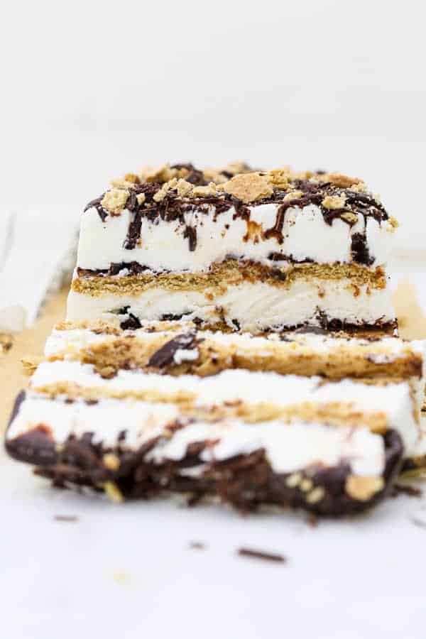 A head on shot of a layered s'mores ice cream cake, there's 3 layers of graham cracker and 3 layers of ice cream with lots of chocolate. A slice of the ice cream cake is layering down and blurred out in the front