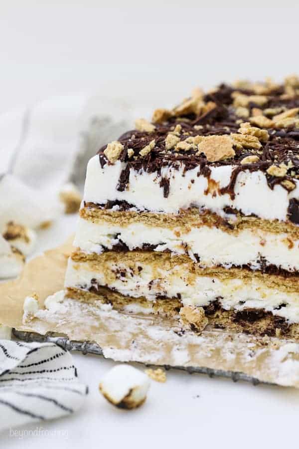A close up shot of a layered s'more ice cream cake with graham cracker, chocolate and marshmallow ice cream. There's a few toasted marshmallow scattered next to it.