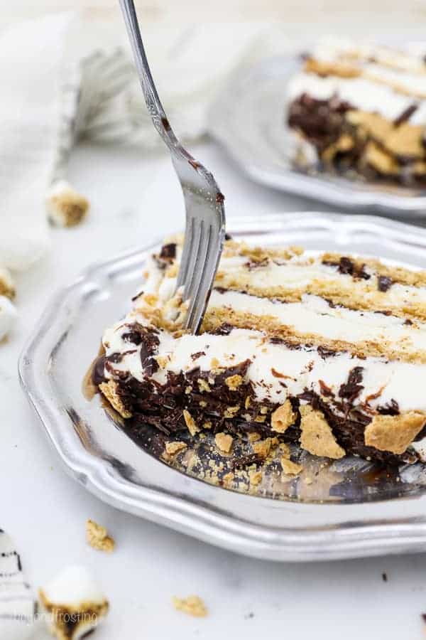 A slice of s'more ice cream cake on a silver vintage plate and a silver fork digging into the slice