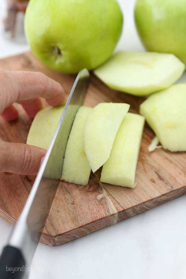 A knife slicing into a peeled green apple on a wooden cutting board
