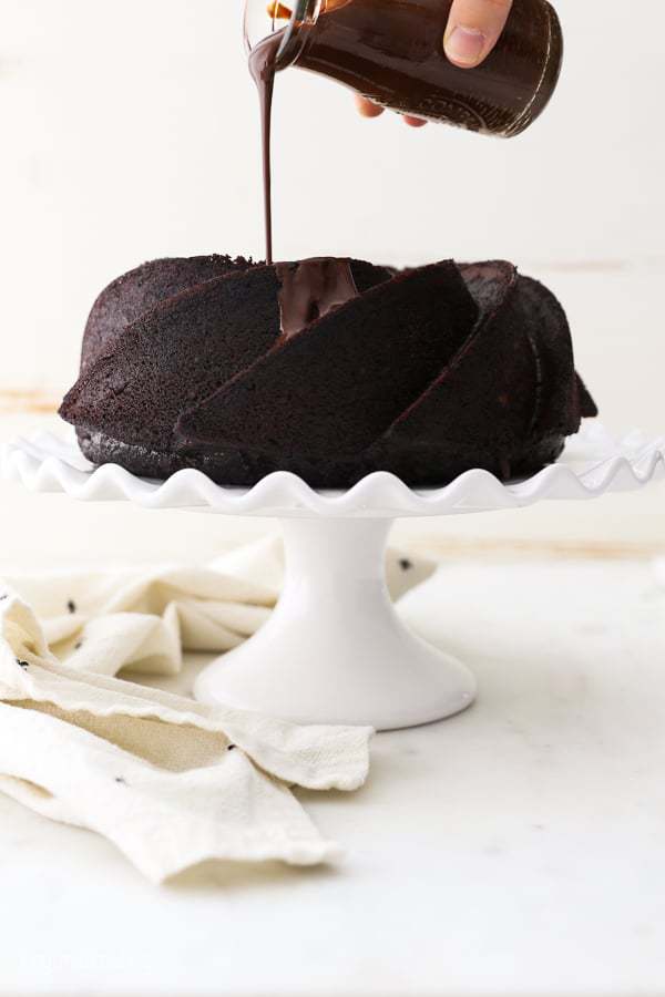 A jar of chocolate ganache being drizzled over a chocolate bundt cake