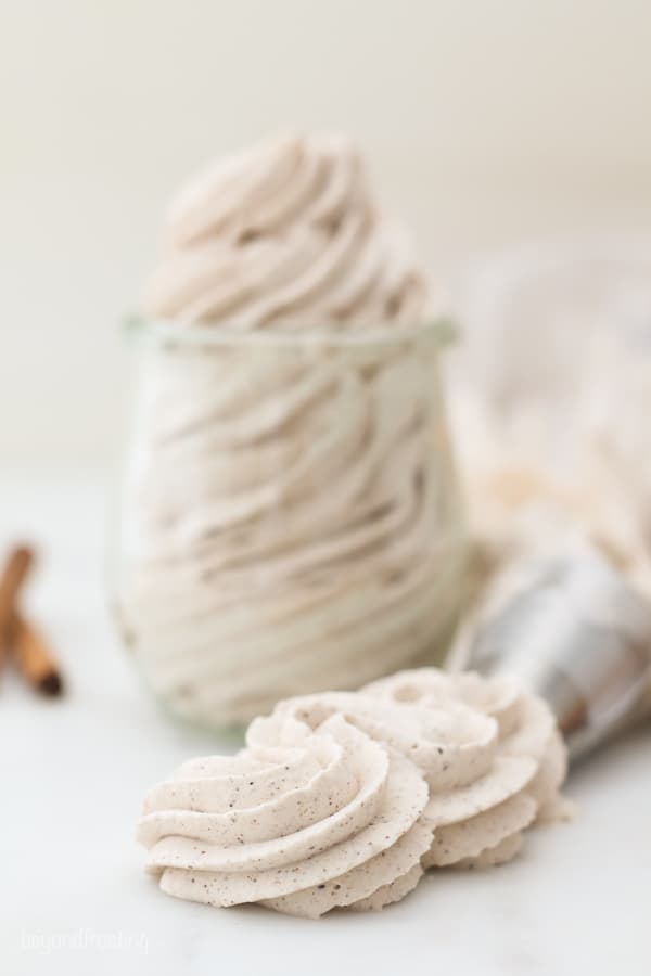 A gorgeous swirl of piped whipped cream with two cinnamon sticks blurred out in the background