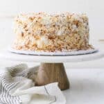 A wide shot of a coconut cake on a marble cake stand draped with a vintage stripe napkin