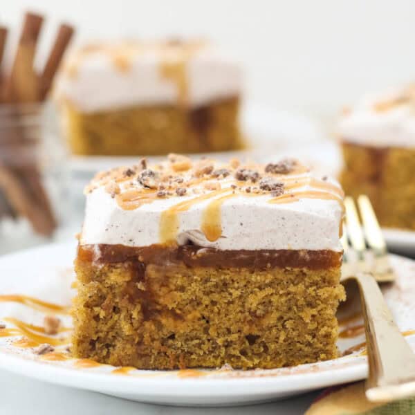A head on shot of a slice of pumpkin poke cake showing the layers of the cake, and a gold fork laying on the white plate