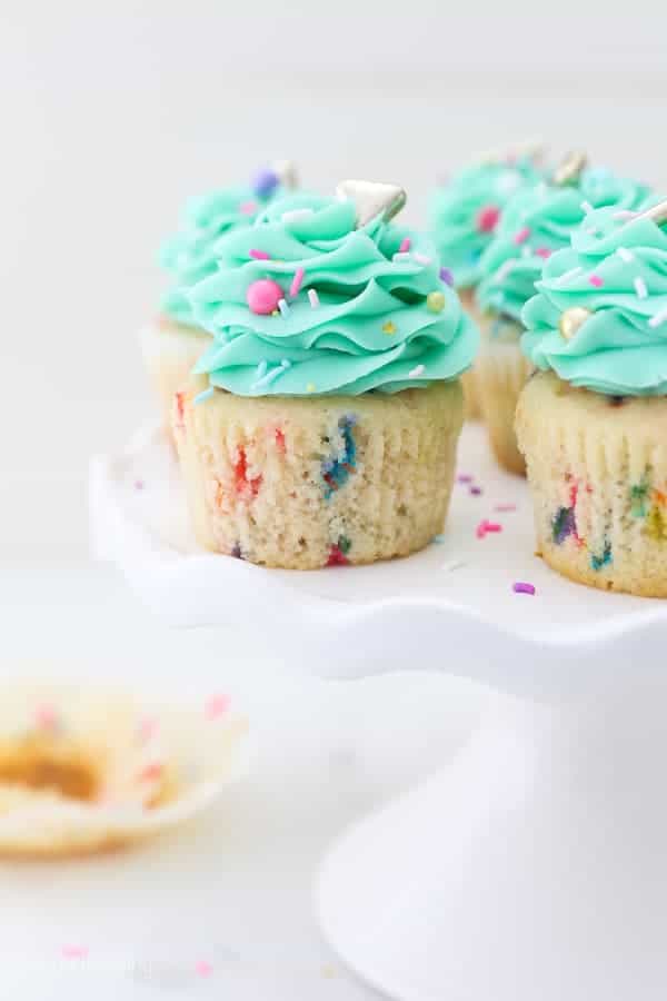 A white ruffled cake stand with funfetti cupcakes with a teal buttercream. The cupcakes are unwrapped.
