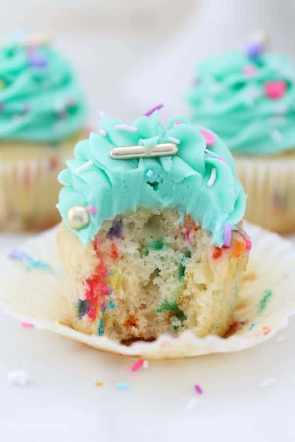 A beautiful funfetti cupcake with a bite taken out of it showing you the inside of the cupcake