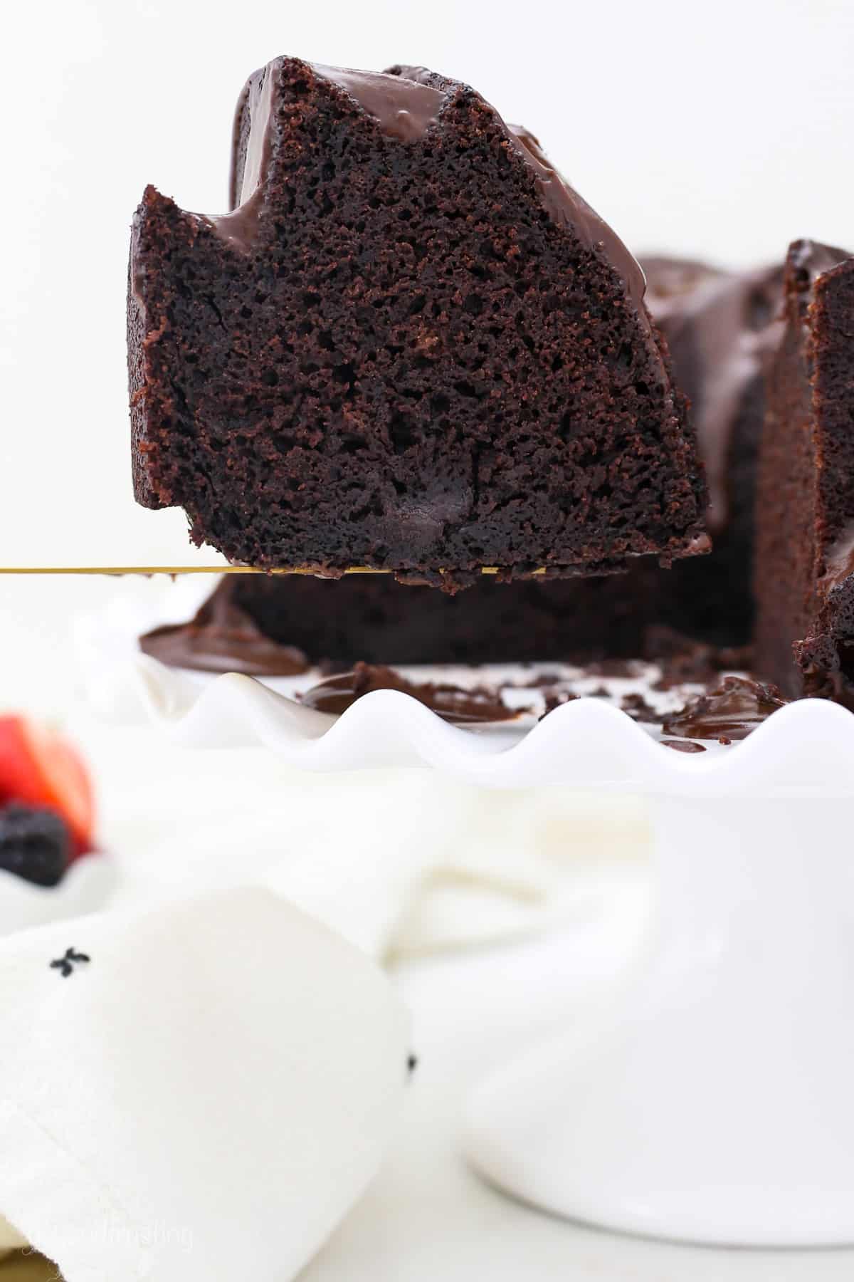 A slice of chocolate bundt cake is lifted from the rest of the cake on a cake stand.