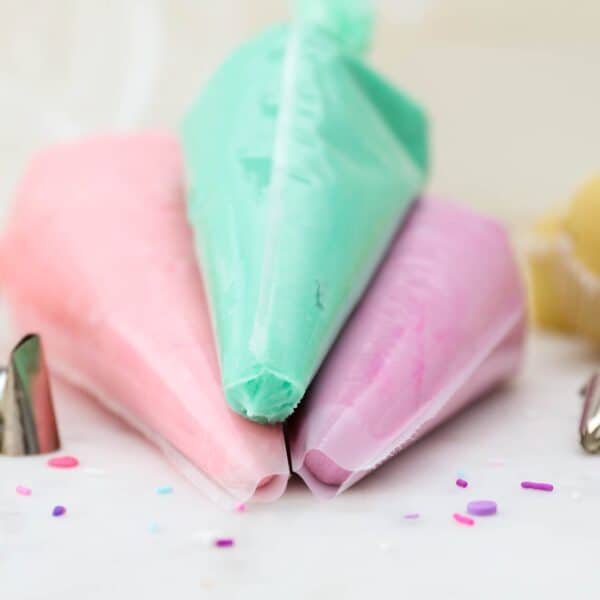 Three piping bags filled with purple, pink, and light turquoise buttercream frosting.