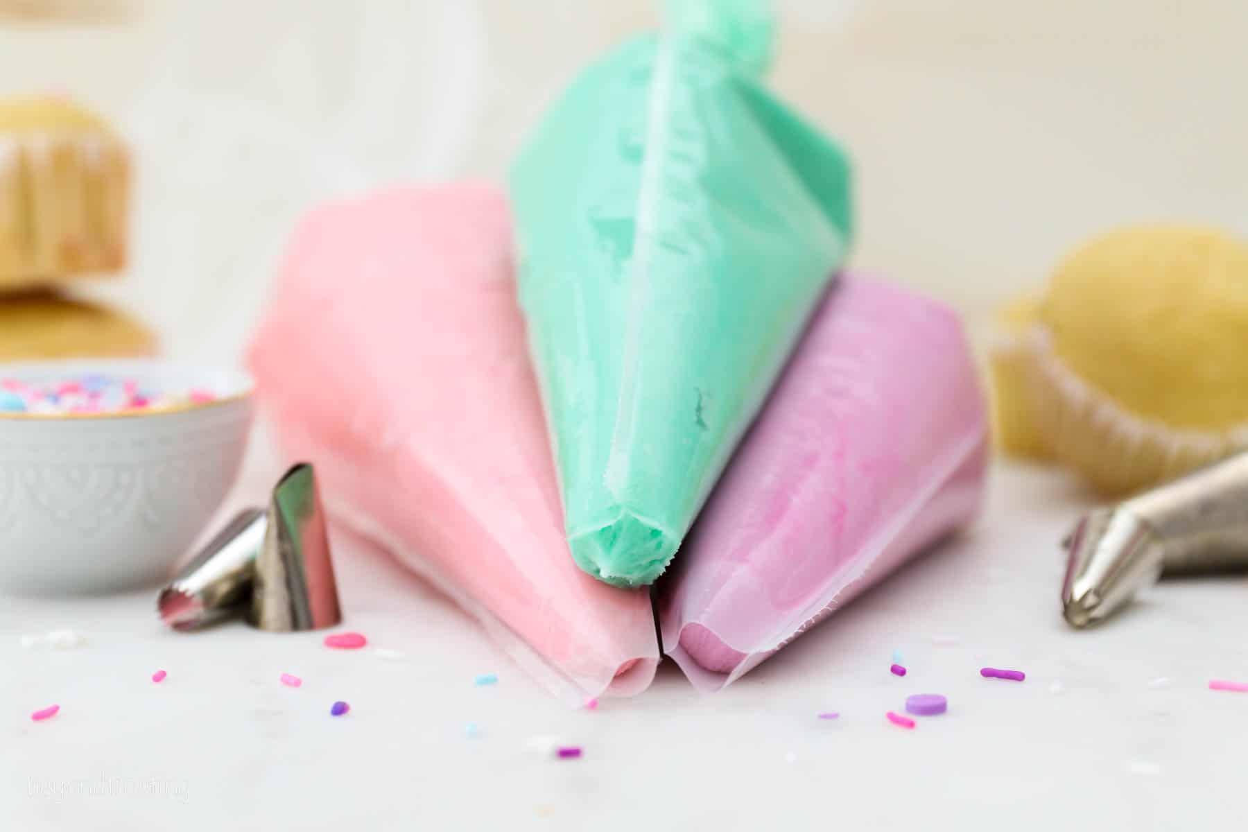 Three piping bags filled with purple, pink, and light turquoise buttercream frosting.