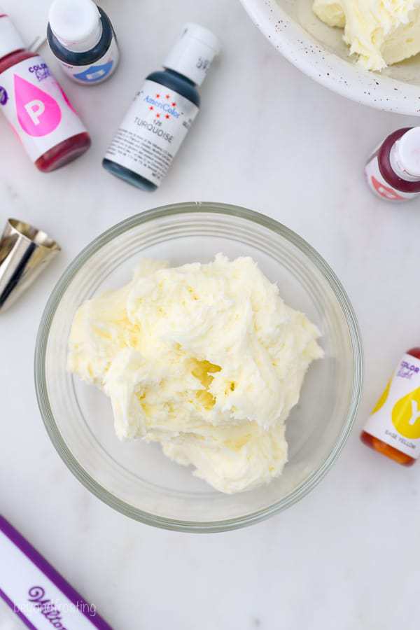 An overhead shot of a bowl of white frosting, and there's piping tips and color gels laying around the bowl