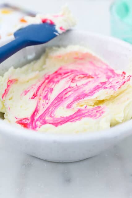 Pink food dye partially mixed into a bowl of vanilla buttercream frosting.