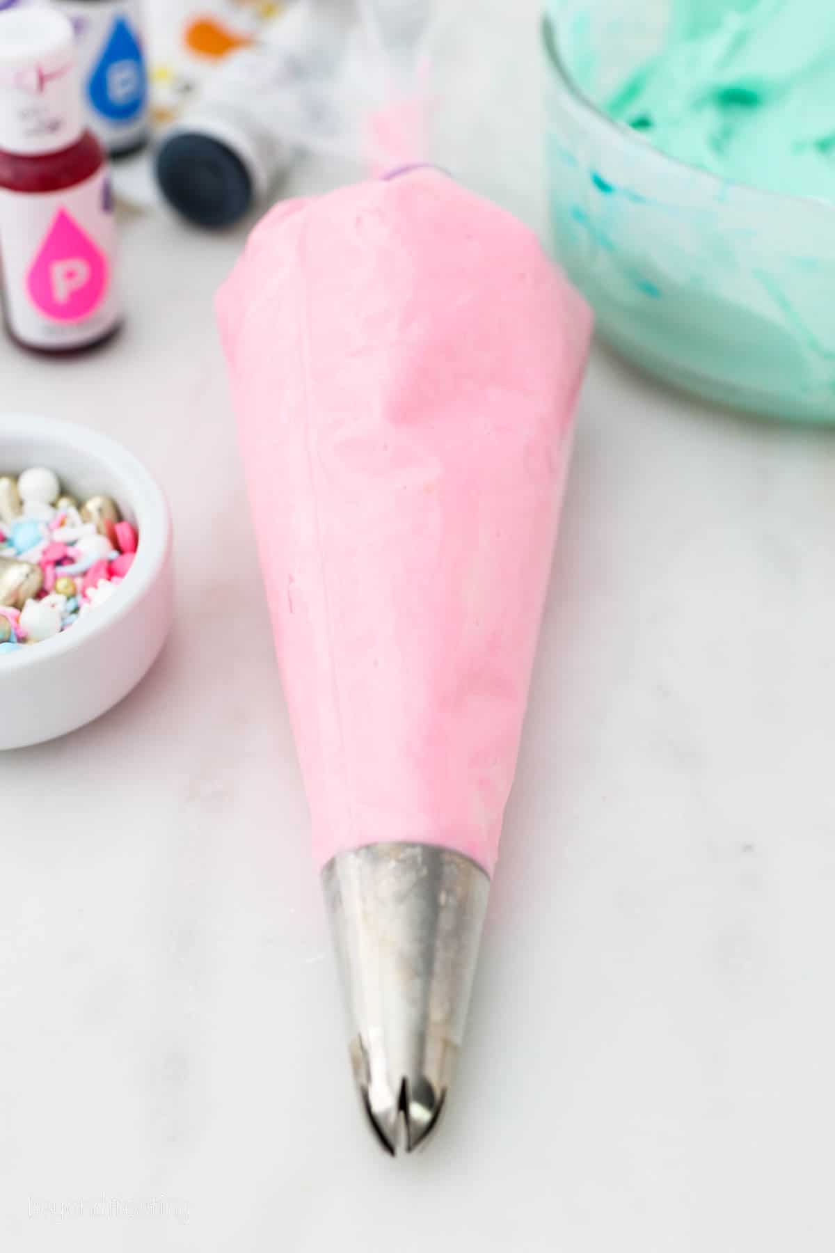 A piping bag with a tip filled with pink buttercream frosting.
