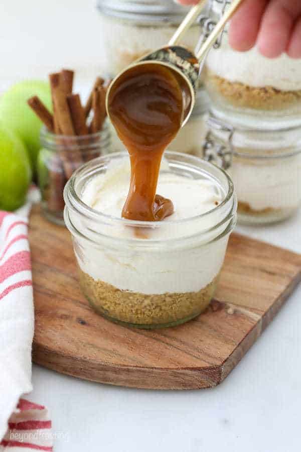 A shot of caramel being drizzled into a mini glass jar filled with cheesecake and crust