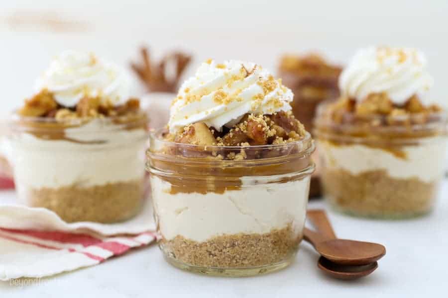 A wide-angle shot of three mini cheesecakes in glass jars with two wooden spoons in the foreground