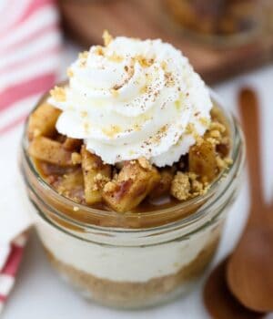 An overhead shot of layered apple cheesecake in a mini glass jar beside two spoons