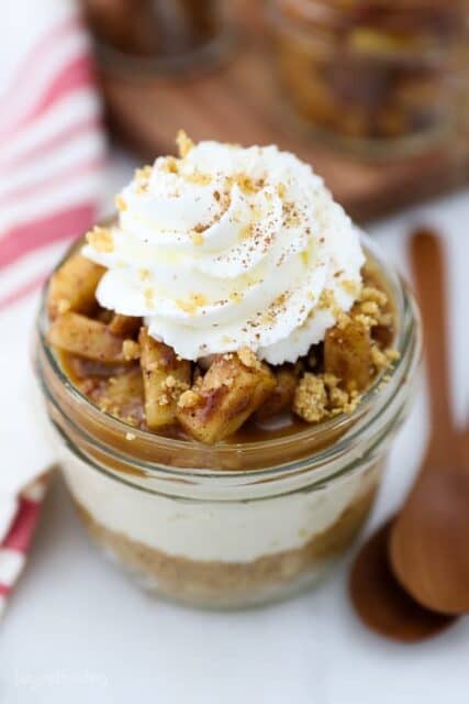 An overhead shot of layered apple cheesecake in a mini glass jar beside two spoons