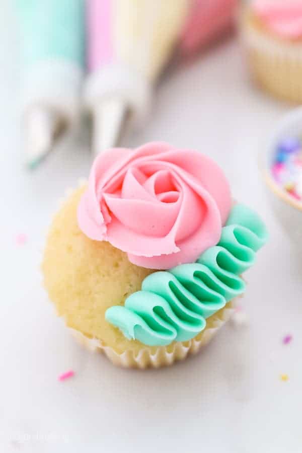 A vanilla cupcake with a pink rose and green ribbon of frosting