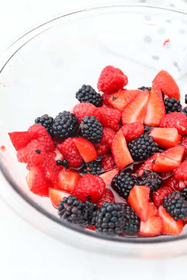 A bowl of fresh strawberries, raspberries and blackberries that are macerated.
