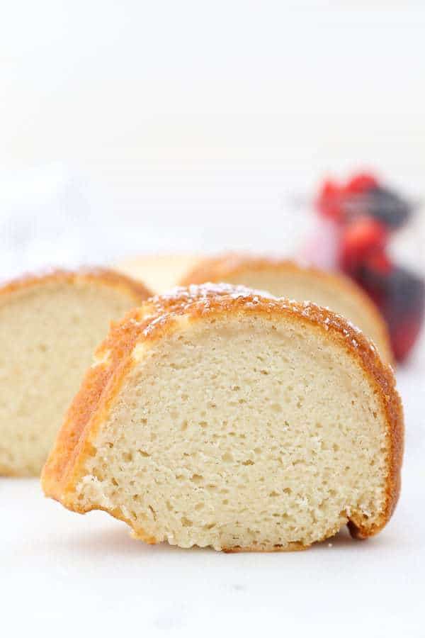 A close up shot of a perfect slice of vanilla bundt cake with some berries blurred out in the background