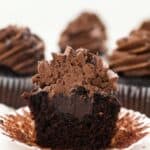 A chocolate cupcake with a chocolate ganache filling is cut in half to show the filling on the inside of the cupcake
