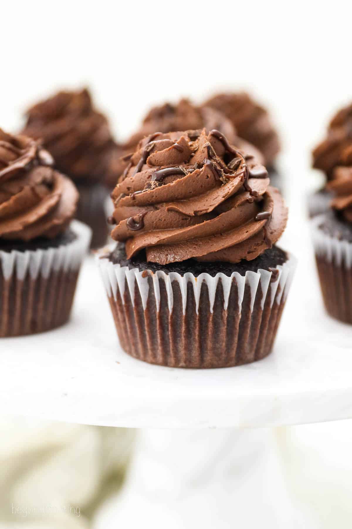 Frosted chocolate ganache cupcakes on a white countertop.