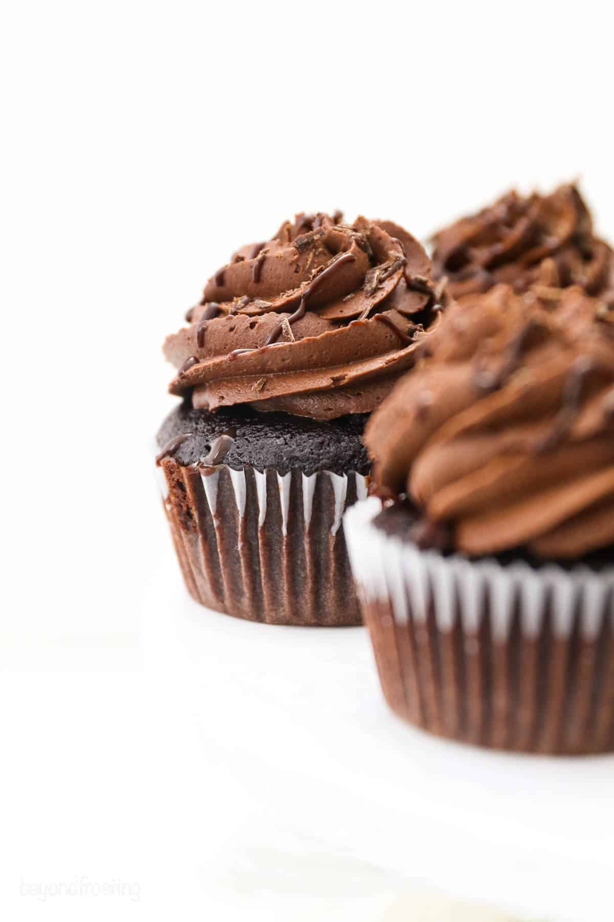 Frosted chocolate ganache cupcakes on a white countertop.