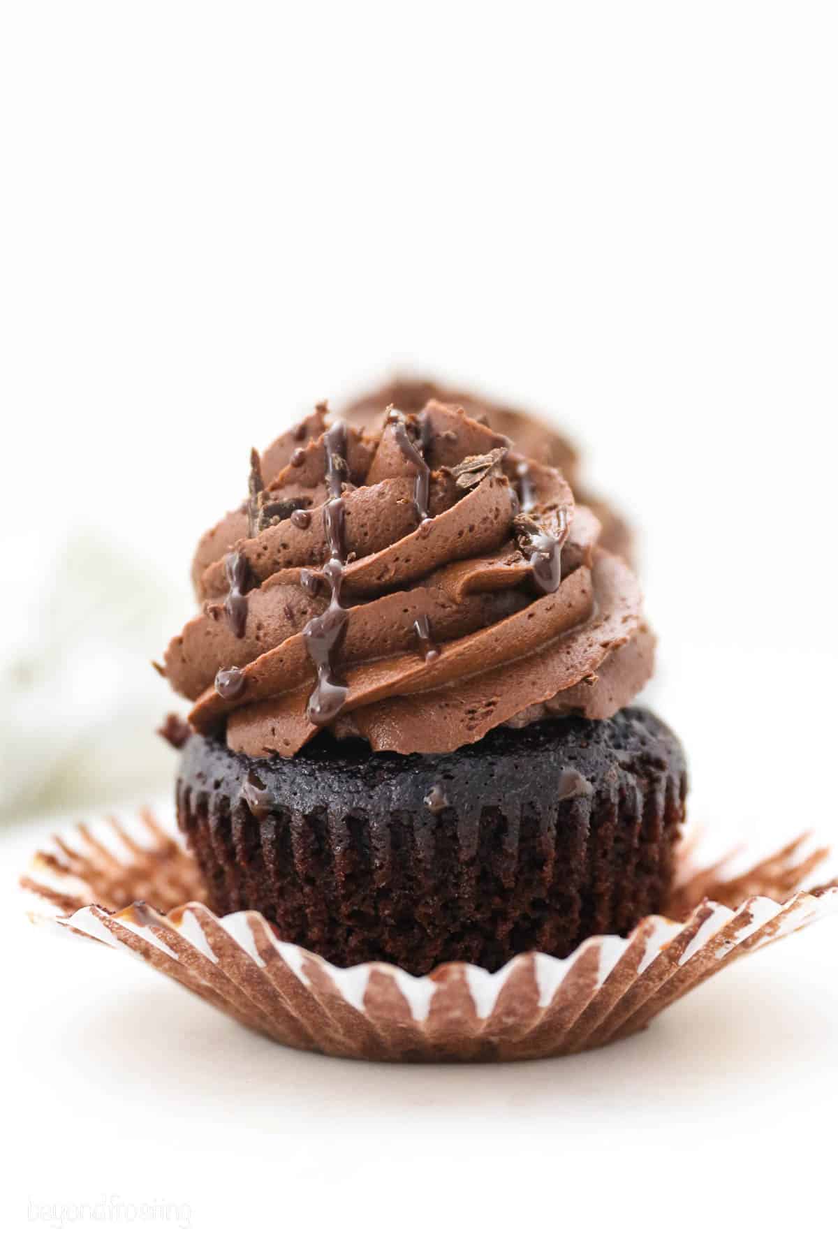 A frosted chocolate ganache cupcake with the liner partially unwrapped and drizzled with chocolate.