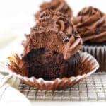 A frosted chocolate ganache cupcake with the liner partially unwrapped with a bite missing.