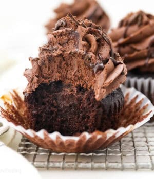 A frosted chocolate ganache cupcake with the liner partially unwrapped with a bite missing.