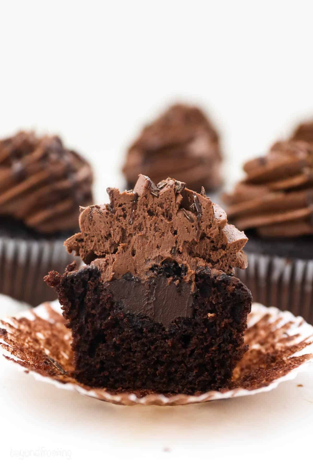 A frosted chocolate cupcake cut in half to reveal the chocolate ganache filling.
