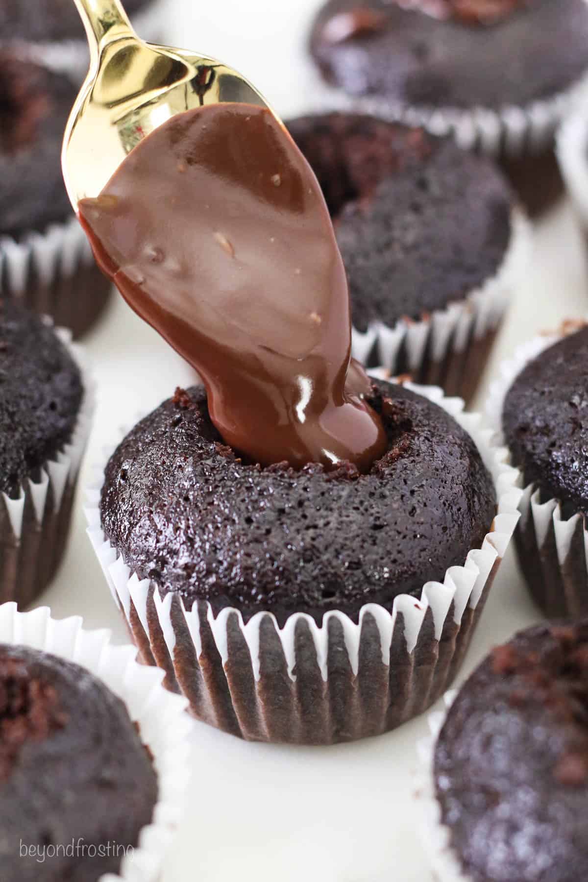 Chocolate ganache is spooned into a hole cut into the center of a chocolate cupcake.