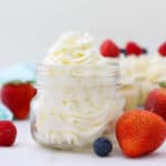 A horizontal image of a small glass jar filled with beautifully piped frosting. The jar is surrounded by berries